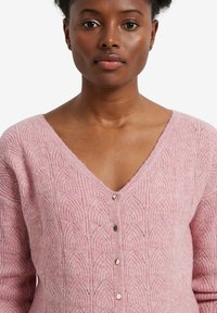 Rosa gestrickte Strickjacke mit einem V-Ausschnitt, die ein strukturiertes Muster aufweist, fünf metallische Knöpfe auf der Vorderseite hat und ein weiches, flauschiges Aussehen besitzt.