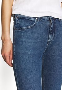 Mörkblå denimjeans med slim fit, 5-fickorsdesign, kopparfärgade knappdetaljer, svaga slitna effekter och en strukturerad tyg-yta.