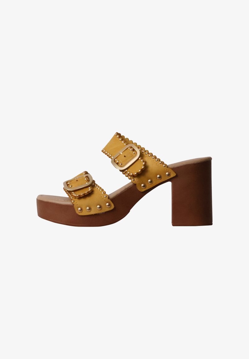 Sandale à talon jaune avec deux brides réglables à boucle, featuring des bords festonnés et des clous décoratifs sur un talon bloc marron.