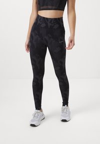 Hoge zwarte leggings met een subtiel textuurpatroon. Gemaakt van rekbare stof voor comfort. Gecombineerd met grijze sportschoenen.