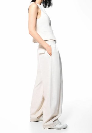 Haut court sans manches beige clair associé à un pantalon beige clair à jambes larges, avec poches latérales et une finition lisse et texturée.