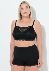 Černé krajkové bralet s nastavitelnými ramínky, který má vlnkované krajkové detaily podél výstřihu, doplněný o černé kraťasy s vysokým pasem.