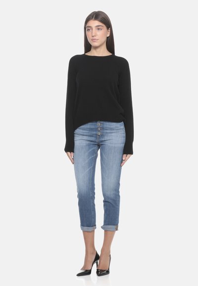 Un pull noir en tricot, un jean en denim bleu clair avec des ourlets roulés, et des chaussures à talon noir. Design simple et ajusté avec un détail de bouton.
