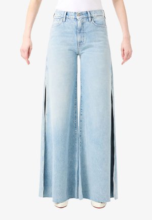 Jeans a gamba larga azzurri chiaro con vita alta e spacchi laterali, indossati con una maglietta bianca e scarpe bianche.