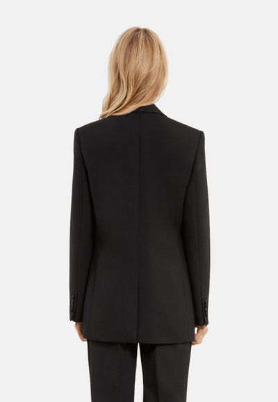 Blazer nero su misura con un design strutturato, rever a punta e polsini con bottoni, realizzato in un tessuto liscio e con una silhouette minimalista.