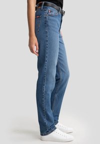 Modri jeans s sproščenim krojem, z višjim pasom, stranskimi in zadnjimi žepi ter poudarki z šivanjem. Oblečeni so z belimi supergami.