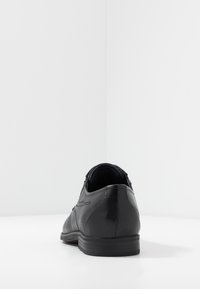 Scarpe oxford in pelle nera con finitura liscia, punta tonda, design minimalista, dettagli laterali testurizzati e tacco basso.