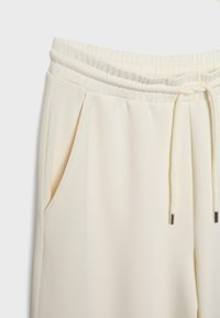 Krämfärgade joggare med elastisk midja, justerbar dragsko och sidofickor. Tillverkade av mjuk, slät tyg med matt yta.