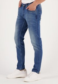 Vidēji zilas džinsu bikses ar izbalējušu apdari, prezentējošas piecas kabatas, pogu un rāvējslēdzēju, kā arī kontrastējošas šuves detaļas.