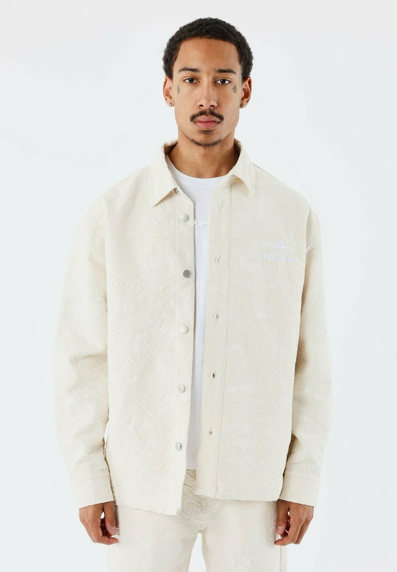 Beige mönstrad skjortjacka med knäppning framtill, med synliga sömmar, en subtil struktur och en liten broderad logotyp på bröstet.