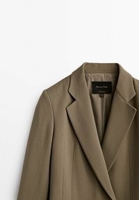 Blazer khaki con design strutturato, rever a forma di nota e una texture liscia. L'interno presenta un'etichetta con i dettagli del marchio.