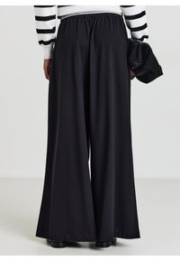 Schwarze weit geschnittene Hosen mit elastischem Bund und glatter Textur, ergänzt durch eine verdeckte Tasche und eine lockere Silhouette.