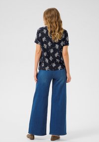 Marineblommig kortärmad topp i kombination med vida blå jeans. Avslappnad passform, mjukt tyg och tydlig blomsterdetaljering över hela plagget.