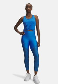 Blue athletic tank top with knotted front and high-waisted blue leggings featuring a textured pattern, paired with white sneakers.