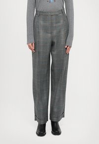 Harmaat ruudulliset housut, joissa on väljä leikkaus, sinisiä ja oransseja yksityiskohtia, korkea vyötärö ja laskostettu etuosa. Mustat nilkkurit näkyvät.