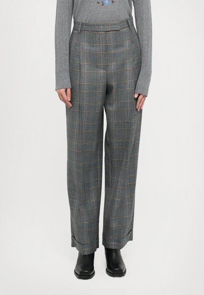 Szare spodnie w kratę o luźnym kroju, z niebieskimi i pomarańczowymi akcentami, wysoki stan i plisowany przód. Widoczne czarne botki za kostkę.