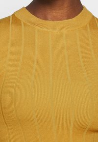 Žebrovaný pletený svetr v barvě hořčicově žluté s kulatým výstřihem a tónovanými vertikálními pruhy. Materiál má texturovaný vzhled.