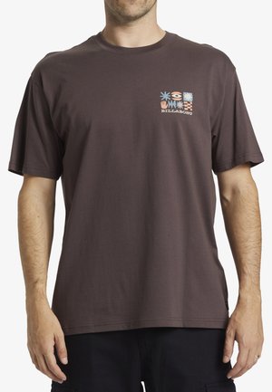 T-shirt en coton brun à manches courtes, ornée d'un graphique carré coloré sur la poitrine gauche, incluant des motifs de fleurs et des symboles.
