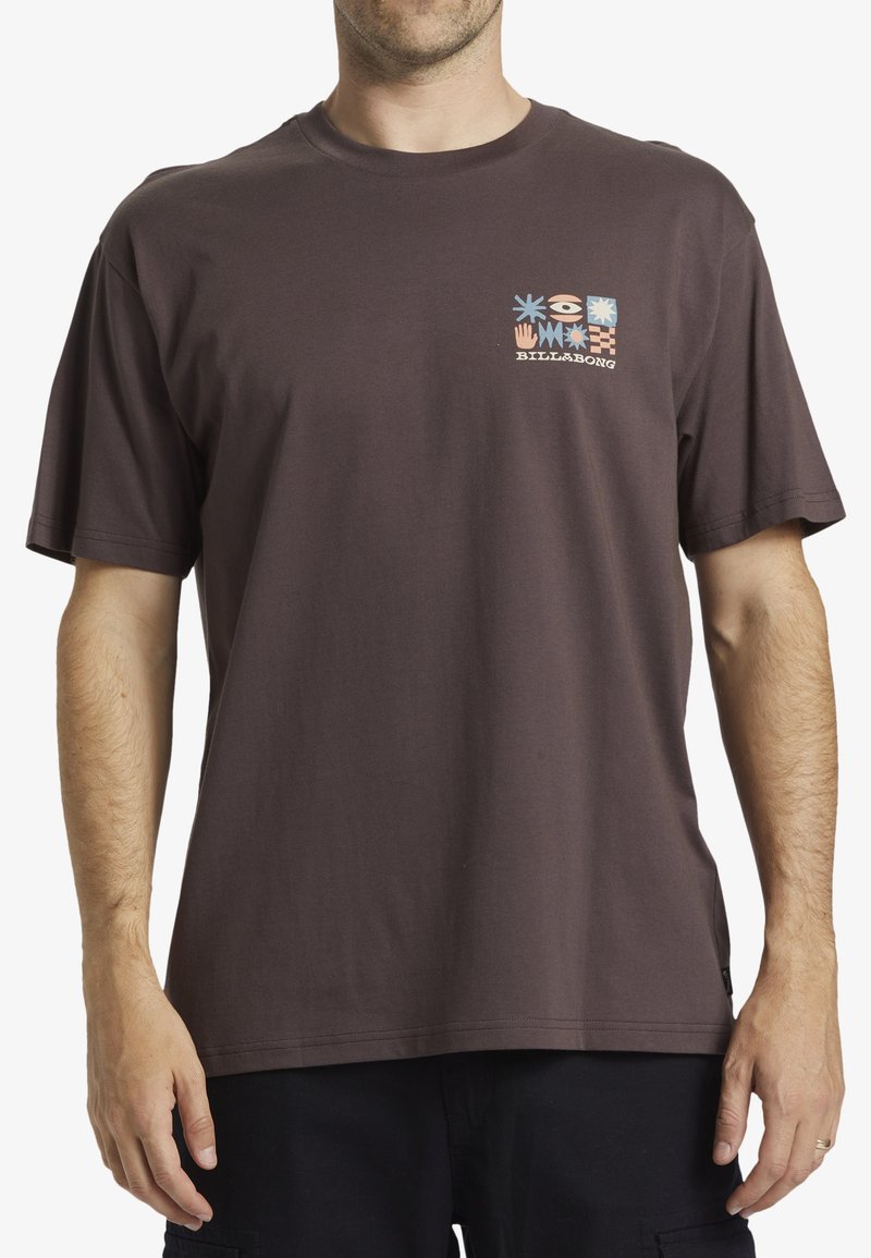 Camiseta de algodón marrón de manga corta, con un gráfico cuadrado colorido en el lado izquierdo del pecho, que incluye patrones de flores y símbolos.