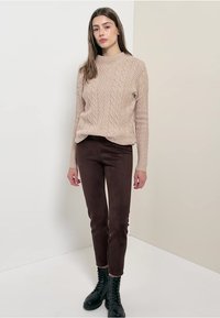 Pull en maille beige avec un col rond, associé à un pantalon marron ajusté et des bottines noires à lacets. Textures lisses, coupe décontractée.