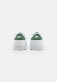 Sneakers bianchi con dettagli in suede verde sul tallone, caratterizzati da un logo testurizzato, una finitura liscia e una silhouette a bassa altezza.