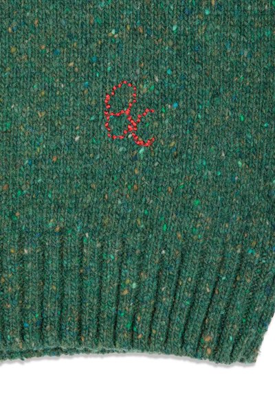 Tissu tricoté vert moucheté avec bord côtelé et petites lettres rouges brodées "Ae" près du centre.