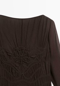 Robe marron foncé avec un tissu texturé, une broderie complexe et des fronces au niveau de l'encolure et sur l'ensemble du vêtement.