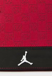 Tessuto rosso con un motivo intrecciato dei numeri "23", accentuato da una parte inferiore in pelle nera e da un logo Jumpman bianco.