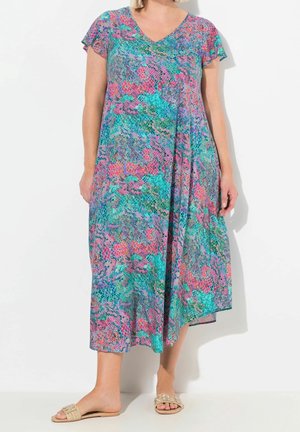 Kvinde iført en ærmeløs, V-hals, multifarvet, mønstret midikjole med beige slip-on sandaler mod en hvid baggrund.