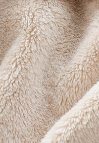 Nahaufnahme von weichem, cremefarbenem Fleece-Stoff, der eine dichte, flauschige Textur und sanfte Falten zeigt.