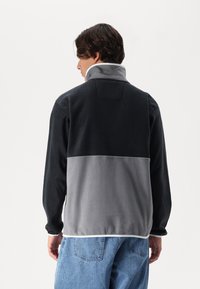 Fleece jacket featuring a two-tone design with a black upper section and a gray lower section. High collar and soft texture.