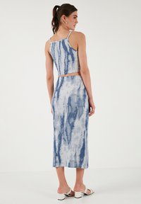 Dvoudílný outfit skládající se z upnutého crop topu a midi sukně, vyrobený z texturované látky s modro-světlým šedým tie-dye vzorem.
