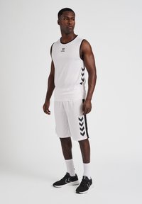 Hvid atletisk tank top og shorts med sorte accenter og chevronmønster på siderne, parret med sorte sportsko og hvide sokker.