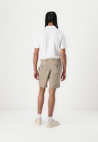 Beige shorts made of lightweight fabric, featuring a tailored cut, two back pockets, and a white polo shirt with short sleeves.