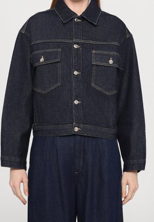 Woman wearing dark blue denim jacket with buttoned flap chest pockets and matching wide-leg denim pants.