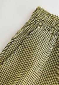 Checked fabric shorts featuring a yellow and navy blue pattern, elastic waistband, and soft texture. Geometric design with small squares.