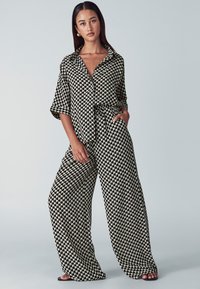 Black and white patterned jumpsuit with a collared neckline, button closure, loose sleeves, and wide leg design, featuring pockets.