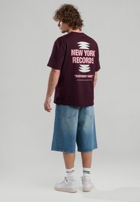 Burgundy graphic t-shirt with  “NEW YORK RECORDS” in pink on the back, paired with light blue denim shorts and white sneakers.