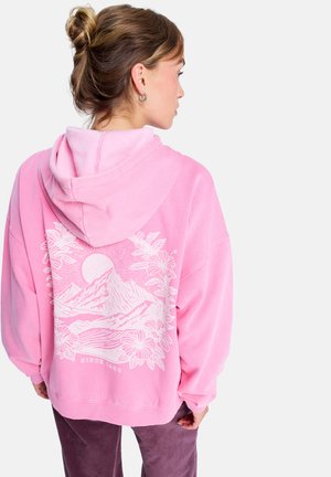 Sweatshirt rose en tissu doux, avec un grand motif blanc représentant des montagnes et un soleil au dos, au design ample et avec capuche.