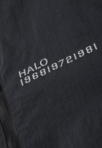 Czarny materiał o teksturowanej powierzchni. Białe nadrukowane napisy obejmują "HALO" oraz numery "196819721981" wzdłuż jednej strony.