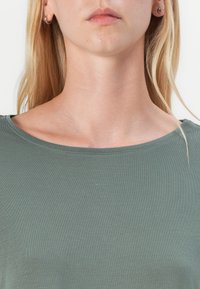 Grønn kortermet topp med rund hals, laget av mykt, teksturert stoff. Har en smal passform som forsiktig former kroppen.