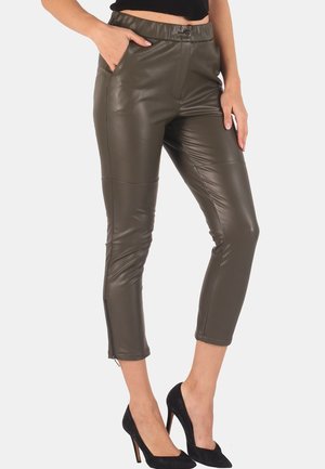 Olive green faux leather fitted pants with a high waist, side pockets, and ankle zippers, paired with black high-heeled shoes.