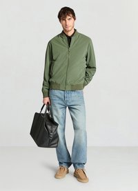 Olive green bomber jacket with a zipper, ribbed cuffs, and collar. Light blue straight-leg jeans, beige shoes, and a black leather tote bag.