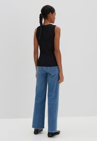 Top noir sans manches associé à un jean bleu décontracté à taille haute et jambes larges. Tissu lisse, coupe décontractée et design simple. Des chaussures noires complètent le look.