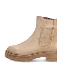 Bottine en suédine beige à semelle épaisse et panneau élastique avec un motif en grille sur fond blanc.