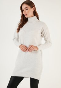 Lys grå, ribbet turtleneck sweater med lange ærmer, blød tekstur og en lidt længere rygkrave. Egnet til afslappet brug.