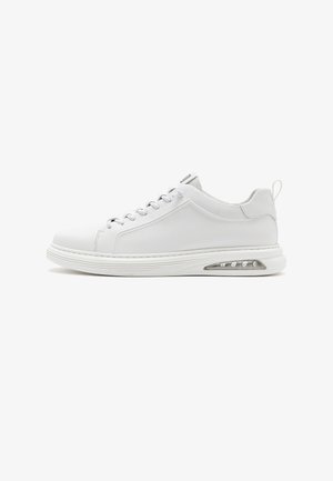 Zapatilla baja blanca con cordones en la parte delantera, suela acolchada, cámara de aire visible en el talón y lengüeta en la parte trasera.