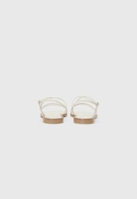 Sandaă cu curele, cu un partea superioară de crem deschis, talpă din lemn plat și cataramă ajustabilă, având un design minimalist și o textură netedă.