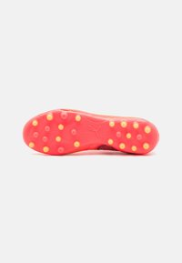 Suela de bota de fútbol en rojo brillante con tapones amarillos, presentando un patrón texturizado y un logo. El material parece duradero para ofrecer tracción.