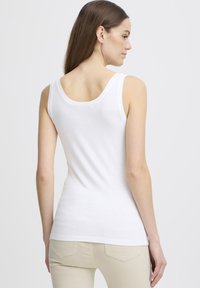 Valge tank top, mis on valmistatud pehmest puuvillast, omades madala seljaga disaini, kitsast istuvust ja ilma nähtavate mustrite või aksessuaarideta.